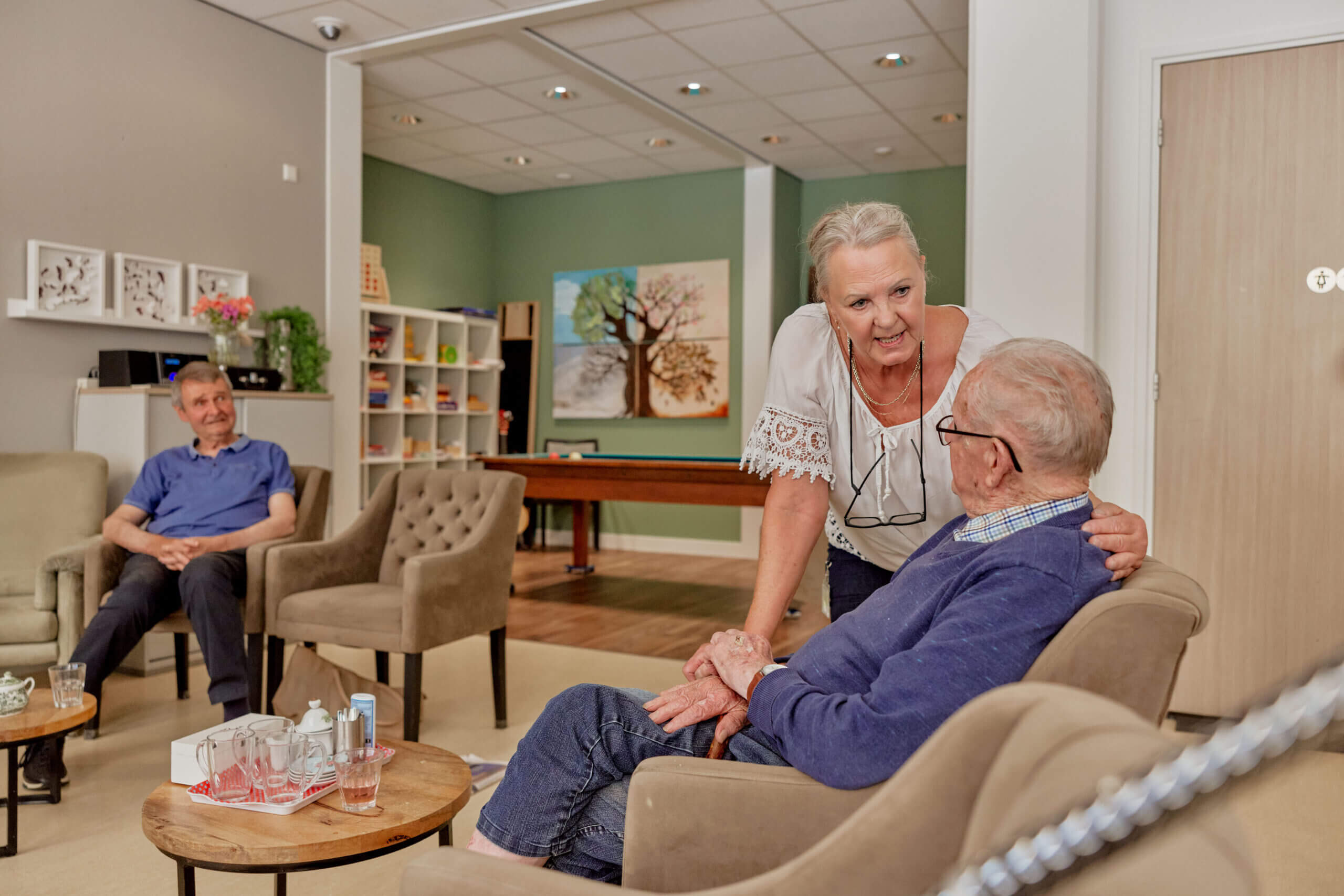Woonkamer verzorgingshuis, man in stoel, vrouwelijke medewerker